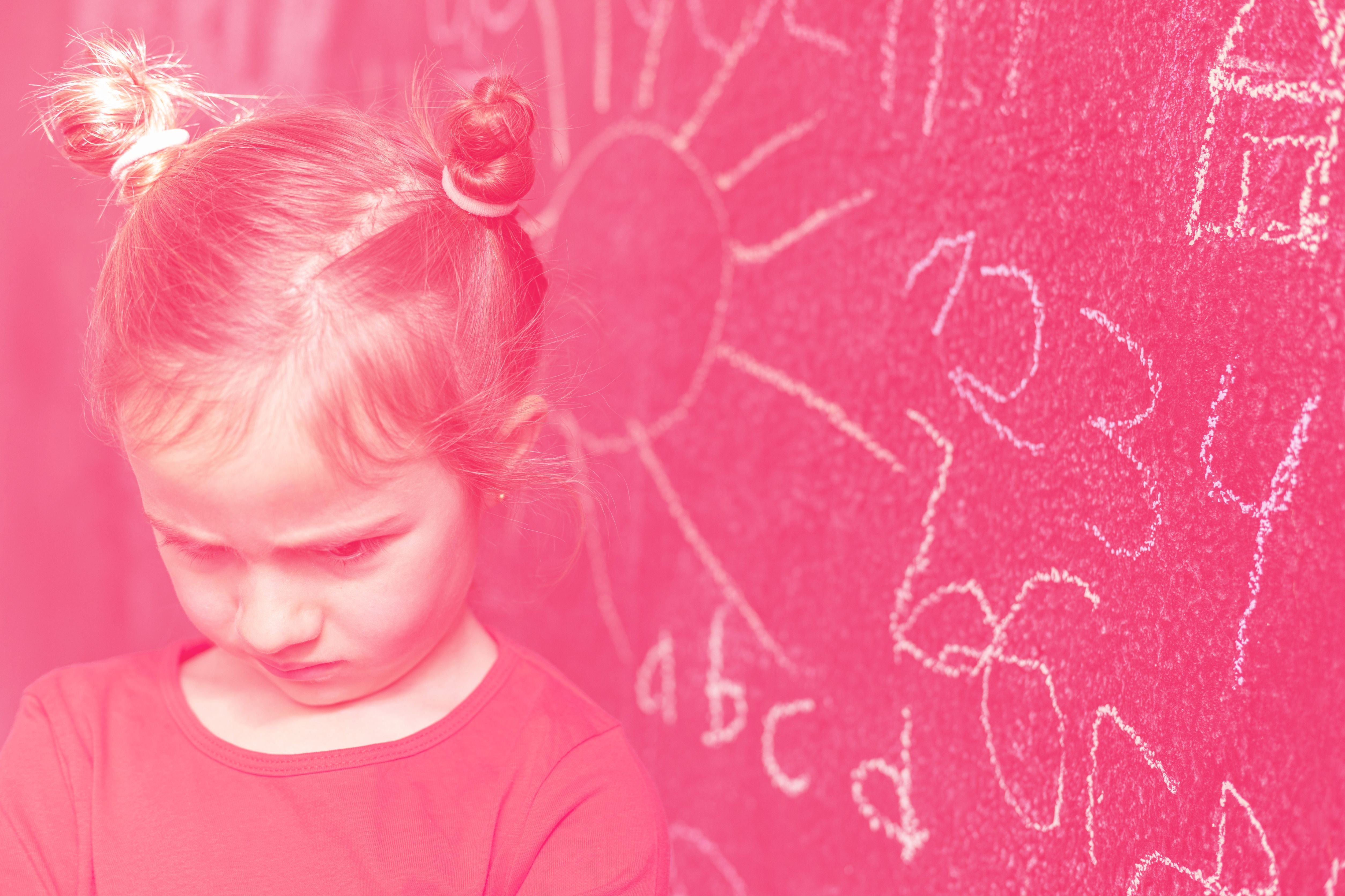 bambina crucciata guarda in basso di fronte a una lavagna scolastica